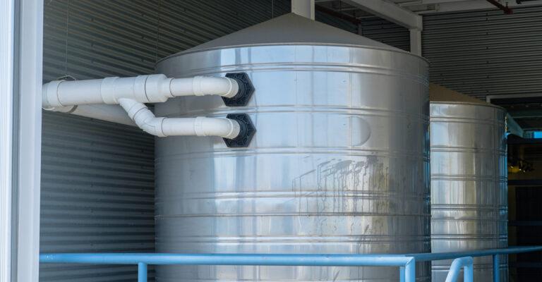 A large stainless-steel rain capture tank sits behind railing. There's another tank behind it, and both connect to pipes.