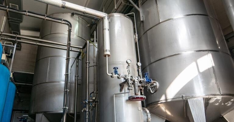 Multiple blue and metallic storage tanks connect to each other. There is water dripping on the floor.