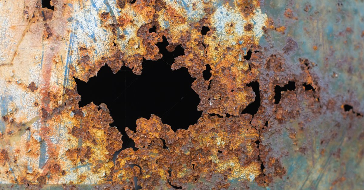 A close-up view of a steel tank with a hole in it because of corrosion. The hole is surrounded by discoloration.