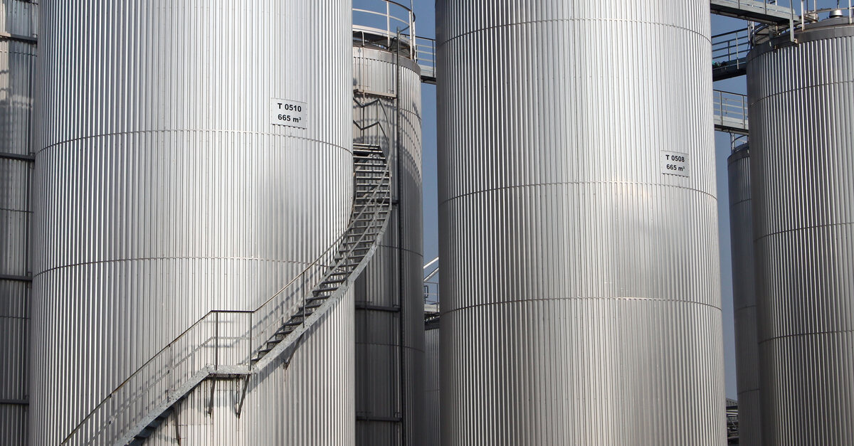 Multiple tall storage tanks stand next to each other, connected by walkways. There are staircases climbing one tank.